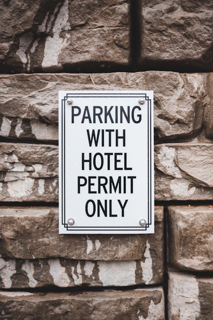 A weathered metal sign mounted on a post in front of a whitewashed wall, indicating a parking restriction with the message 'This space reserved 24 hours'. The sign shows signs of rust, peeling paint, and corrosion, with visible screws securing it to the post. The surrounding environment suggests an urban setting, relevant to house removals or relocation services such as those offered by Hampstead Removals. The sign's condition reflects typical street-side signage that may impact parking arrangements during a home relocation or furniture transport process, emphasizing the importance of understanding parking permits and access when planning NW3 flat removals. The overall scene captures the context of logistical considerations involved in loading and unloading within restricted parking zones, supporting careful planning for house moving services.